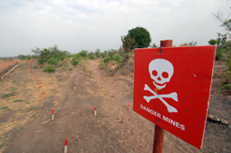 Un terrain vague à l'entrée duquel une affiche rouge avec une tête de mort annonce: Danger, mines.