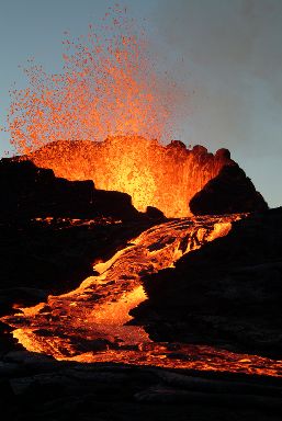 The peak of an erupting volcano with a lava flow cascading down its side.